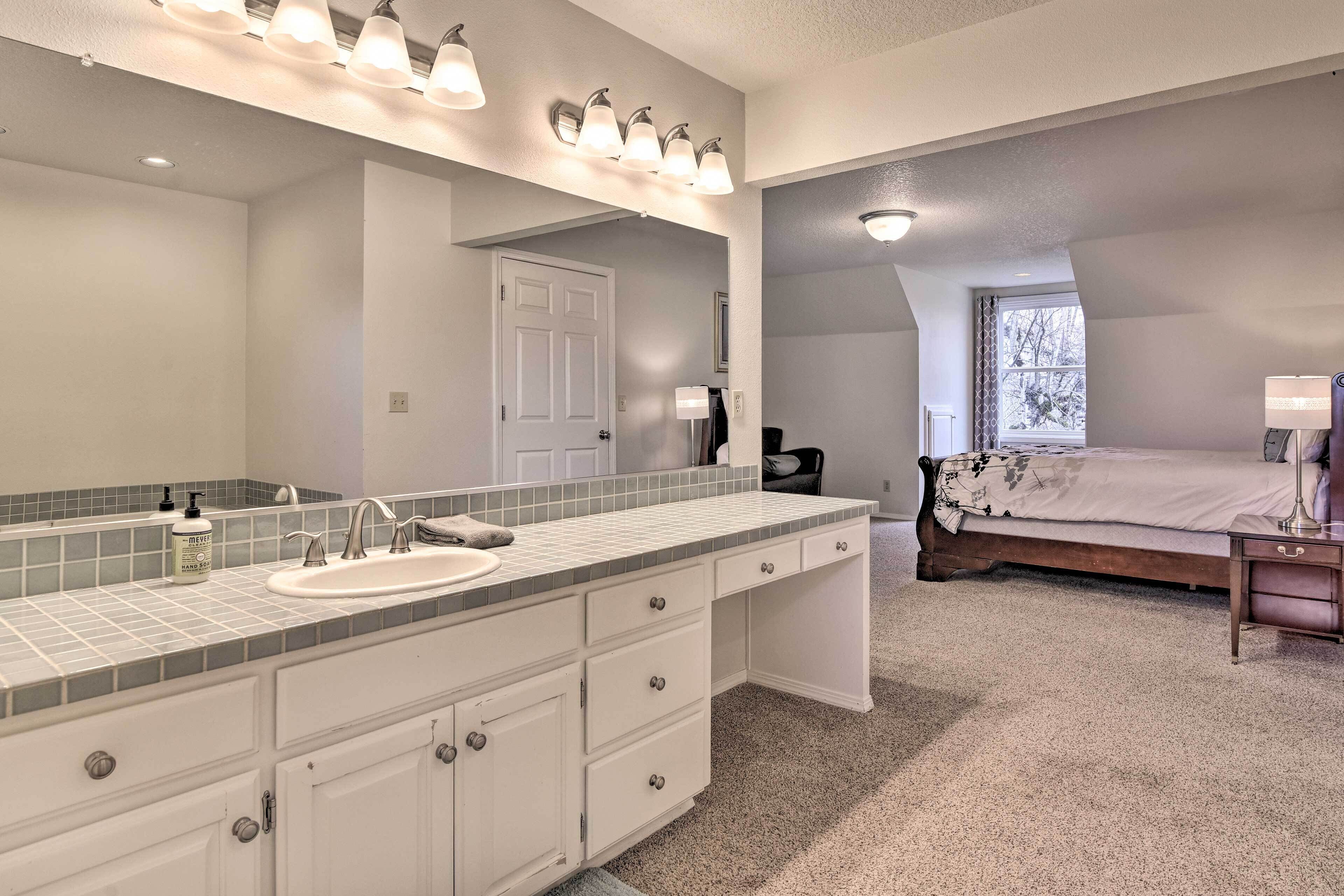 A bathroom with a large mirror, white cabinets, a sink, and a vanity.