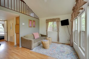 Ein Wohnzimmer mit einer Couch, zwei Beistelltischen, einem gemusterten Teppich, einem Fernseher und einem Fenster mit Vorhängen.