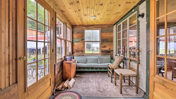A cozy cabin interior with a wooden ceiling, large windows, a striped sofa, and a dining area. - Rustic Roxbury Ski Farmhouse With Trails! (Roxbury)