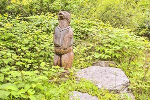 Una estatua de madera de un oso en un entorno natural con follaje denso y rocas.