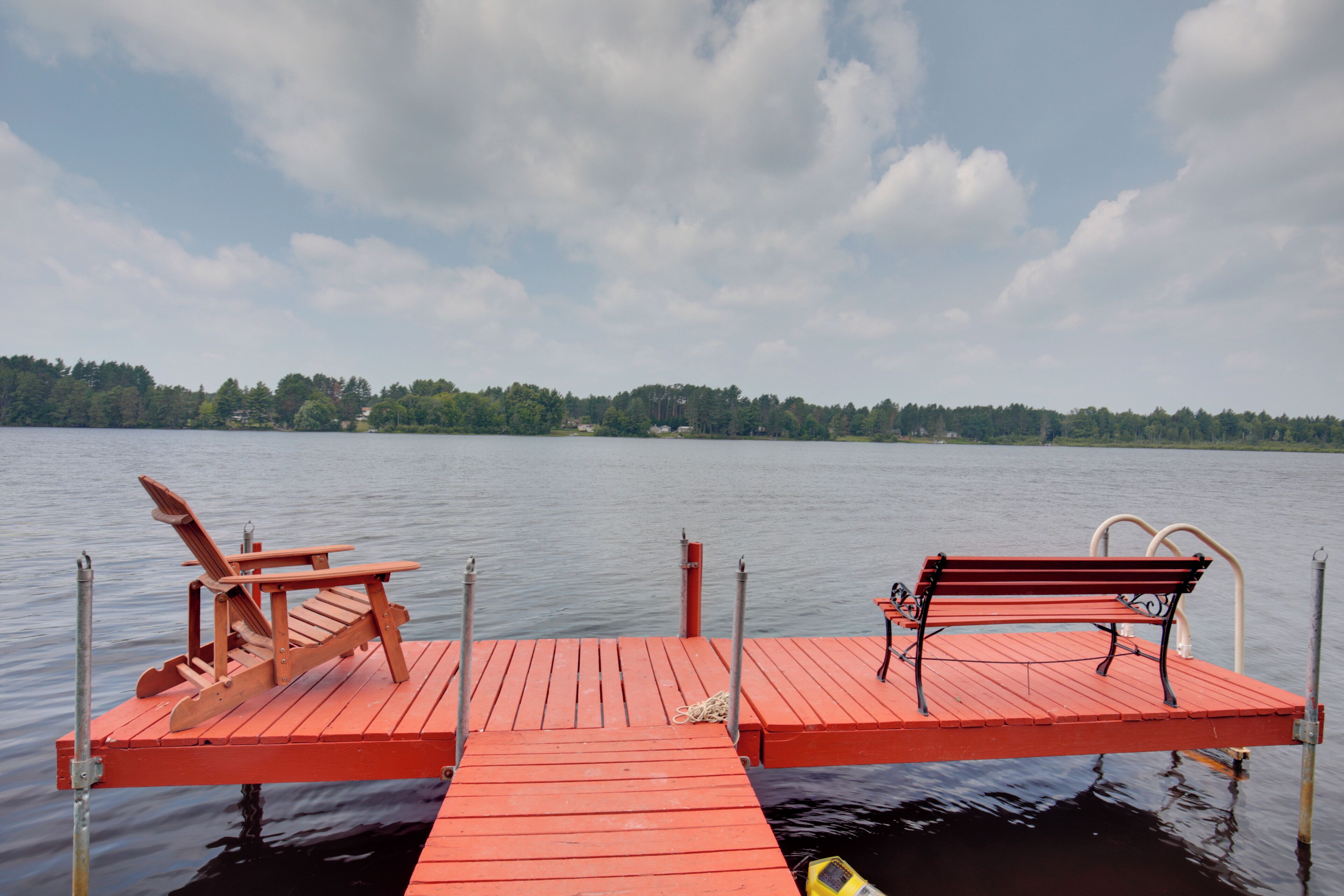 A wooden dock extending into a calm lake with a bench and a chair on it.