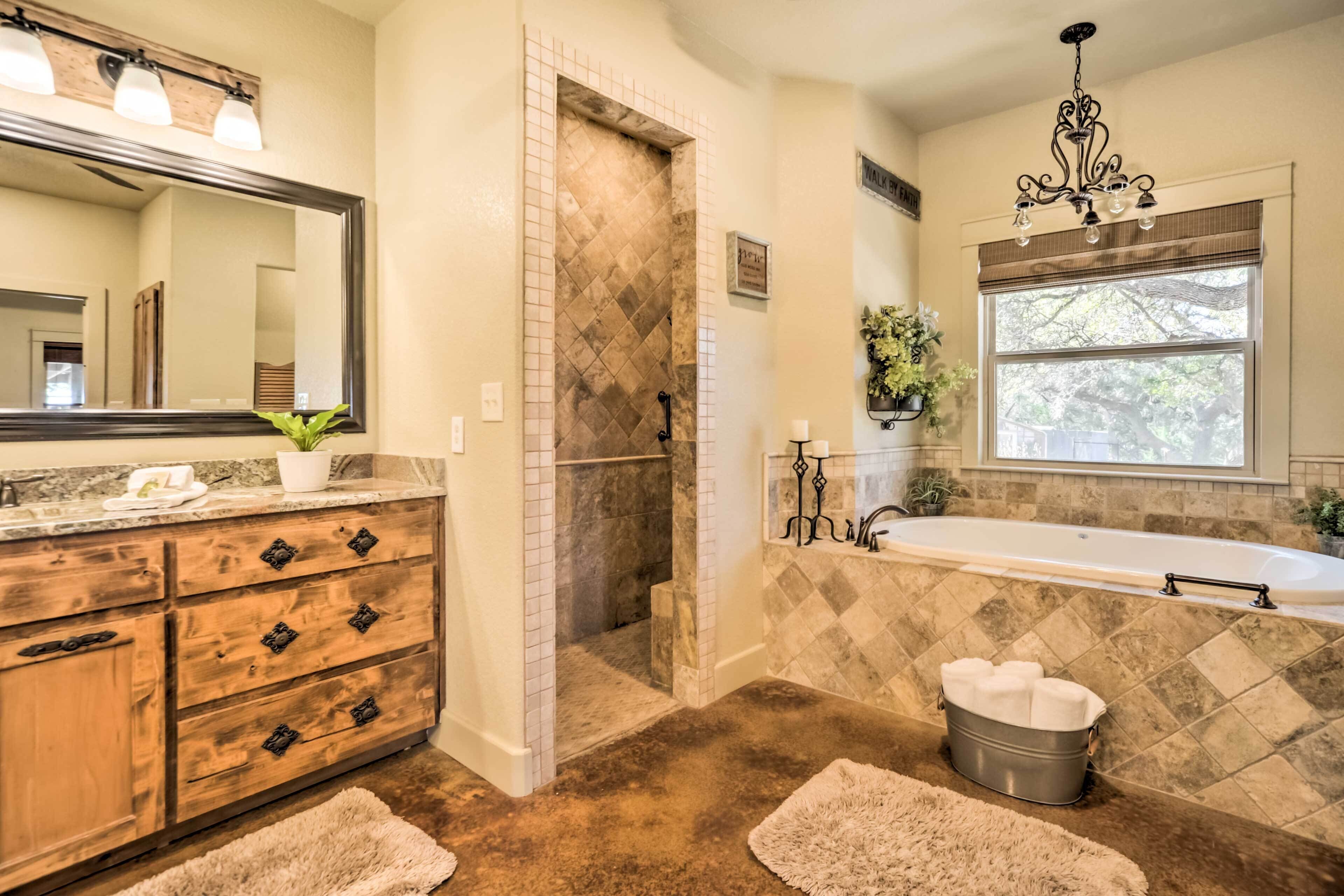 A bathroom with a wooden vanity, a large mirror, a shower with a diamond-patterned tile wall, a bathtub, and a window with a view of trees.
