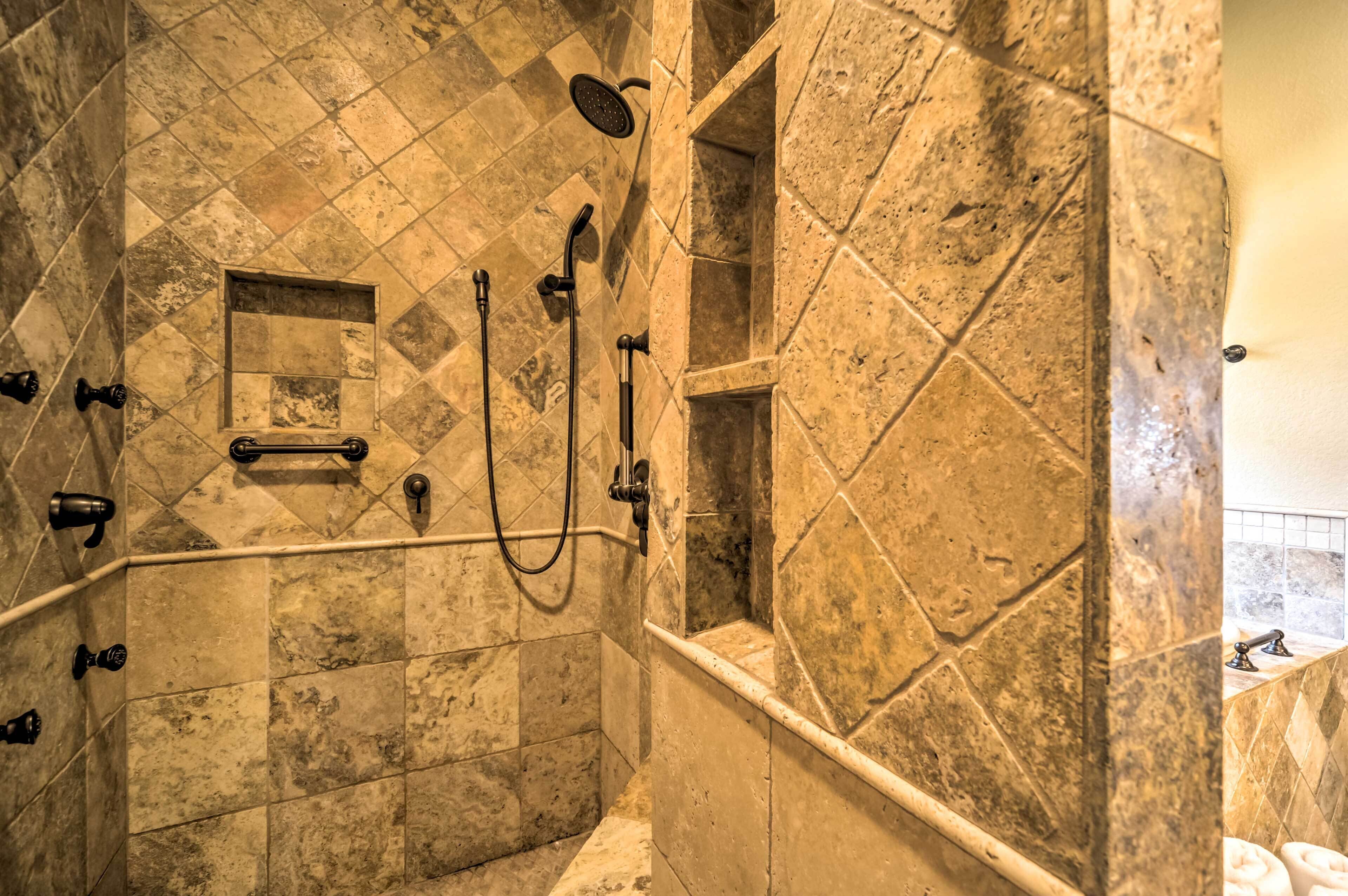 A shower area with a handheld showerhead, a handheld shower nozzle, and a wall-mounted showerhead. There is a small window in the shower area.