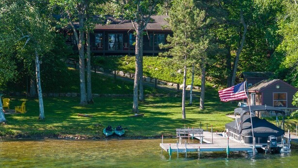 A lakeside property with a dock, a small cabin, and a large house in the background.