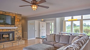 A living room with a stone fireplace, a sectional sofa, and a dining area with a table set for six. - Monticello Home w/ Multi-level Deck on 2 Acres! (Monticello)