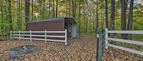 A rustic cabin with a wooden exterior and a metal roof, surrounded by a white fence and a metal gate.