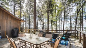 Una terraza de madera con una mesa y sillas, rodeada de árboles altos y vistas al agua.