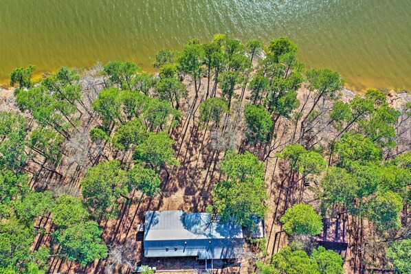 An aerial view of a house surrounded by dense trees near a body of water.