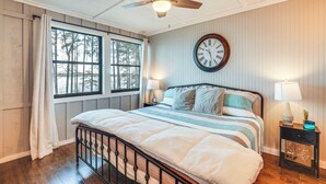 Un dormitorio con una cama, ventilador de techo, un reloj, una ventana y una mesita de noche con lámpara.