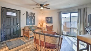 A room with a dark wooden door, a ceiling fan, a large window with curtains, and a wicker chair with cushions. - 4 Mi to Dtwn: Rustic Fort Worth Apt (Fort Worth)