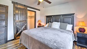 A bedroom with a bed, a ceiling fan, a nightstand, and a door with a rustic design. - 4 Mi to Dtwn: Rustic Fort Worth Apt (Fort Worth)