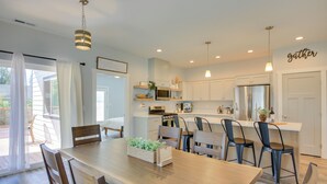 A modern kitchen with white cabinets, a central island with bar stools, and a dining area with a wooden table and chairs. - 3 Mi to Lake Pend Oreille: Home w/ Deck & Yard (Ponderay)