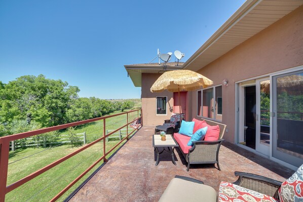 A covered outdoor area with a patio set, a thatched umbrella, and a view of a green landscape.