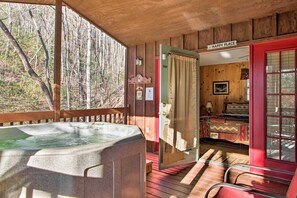 A wooden cabin with a hot tub, a red door labeled "Happy Place," and a bed with patterned bedding. - Private Gatlinburg Cabin: Pet Friendly w/ Hot Tub! (Gatlinburg)