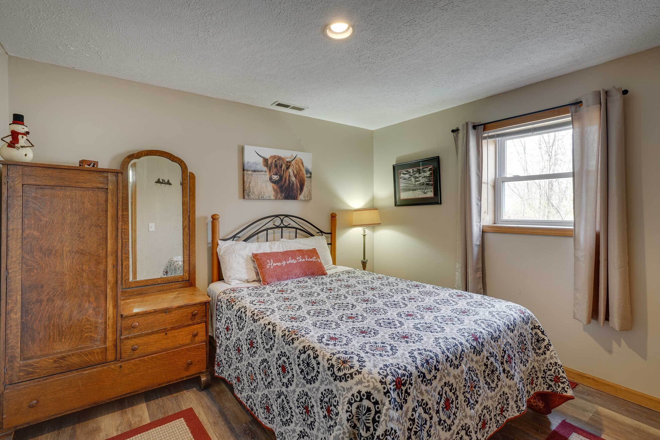 Une chambre à coucher avec un lit, une commode, un miroir, une lampe et une fenêtre avec des rideaux.