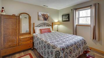 Une chambre à coucher avec un lit, une commode, un miroir, une lampe et une fenêtre avec des rideaux.