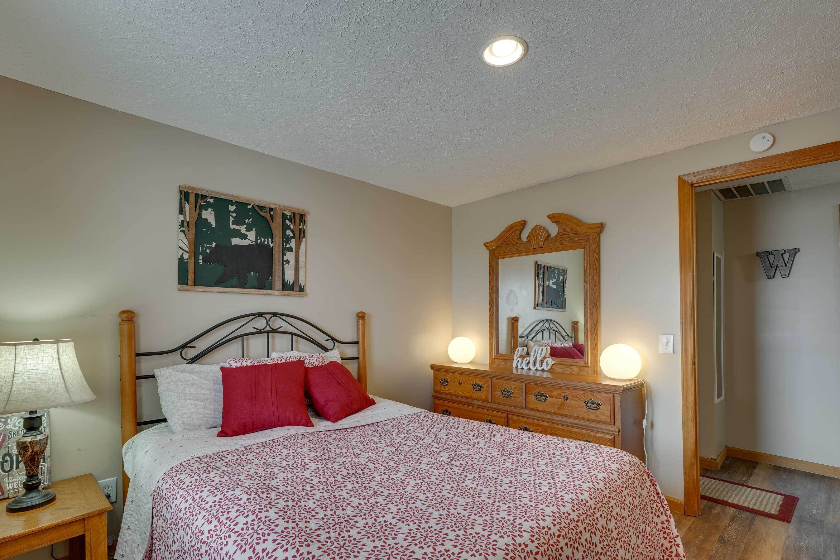 A bedroom with a bed, a nightstand, a dresser, a mirror, and a door.