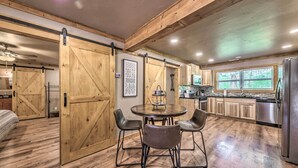 A spacious kitchen with wooden flooring, a dining area with two chairs, and a large sliding barn door. - Ruidoso Cabin w/ Patio - Walk to Midtown! (Ruidoso)