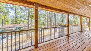 A wooden deck with a railing, overlooking a forested area with cabins. - Ruidoso Cabin w/ Patio - Walk to Midtown! (Ruidoso)