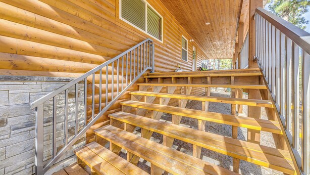A wooden staircase with metal railings leading to a covered area with wooden walls and windows. - Ruidoso Cabin w/ Patio - Walk to Midtown! (Ruidoso)
