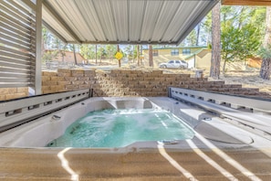 A hot tub under a covered patio with a brick wall and a view of a residential area. - Ruidoso Cabin w/ Patio - Walk to Midtown! (Ruidoso)
