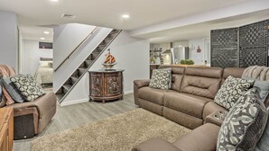 A spacious living room with a brown leather sofa, patterned throw pillows, a wooden side table, and a staircase leading to an upper level. - Saddle Brook Studio With Patio - Near Nyc! (Saddle Brook)