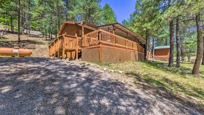 A wooden cabin with a deck, surrounded by pine trees.