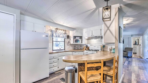 A modern kitchen with white cabinets, a stainless steel refrigerator, a wooden island with chairs, and a hanging light fixture.