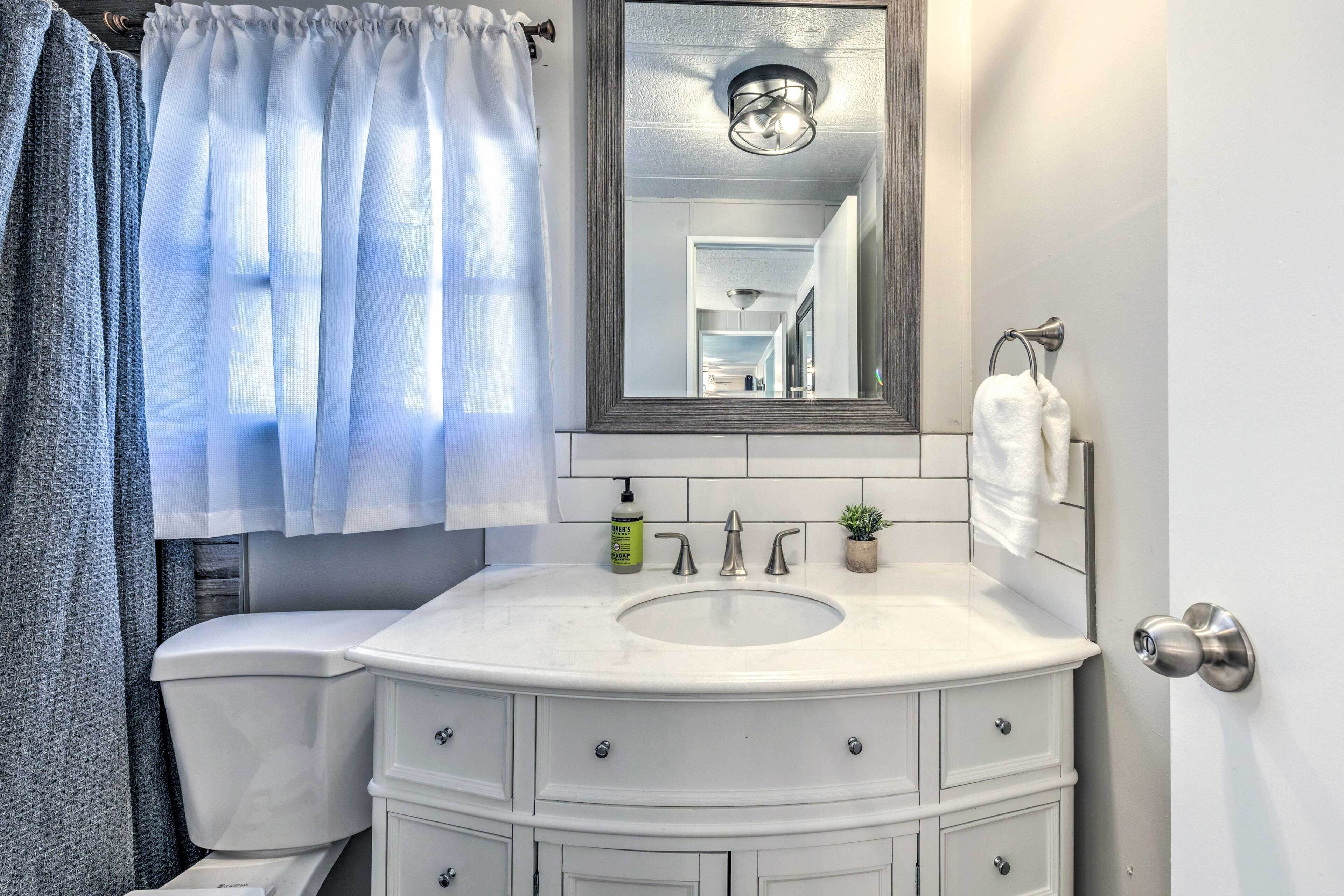 A bathroom with a white sink, vanity, and toilet. There is a mirror above the sink, a towel rack, and a small potted plant on the vanity.