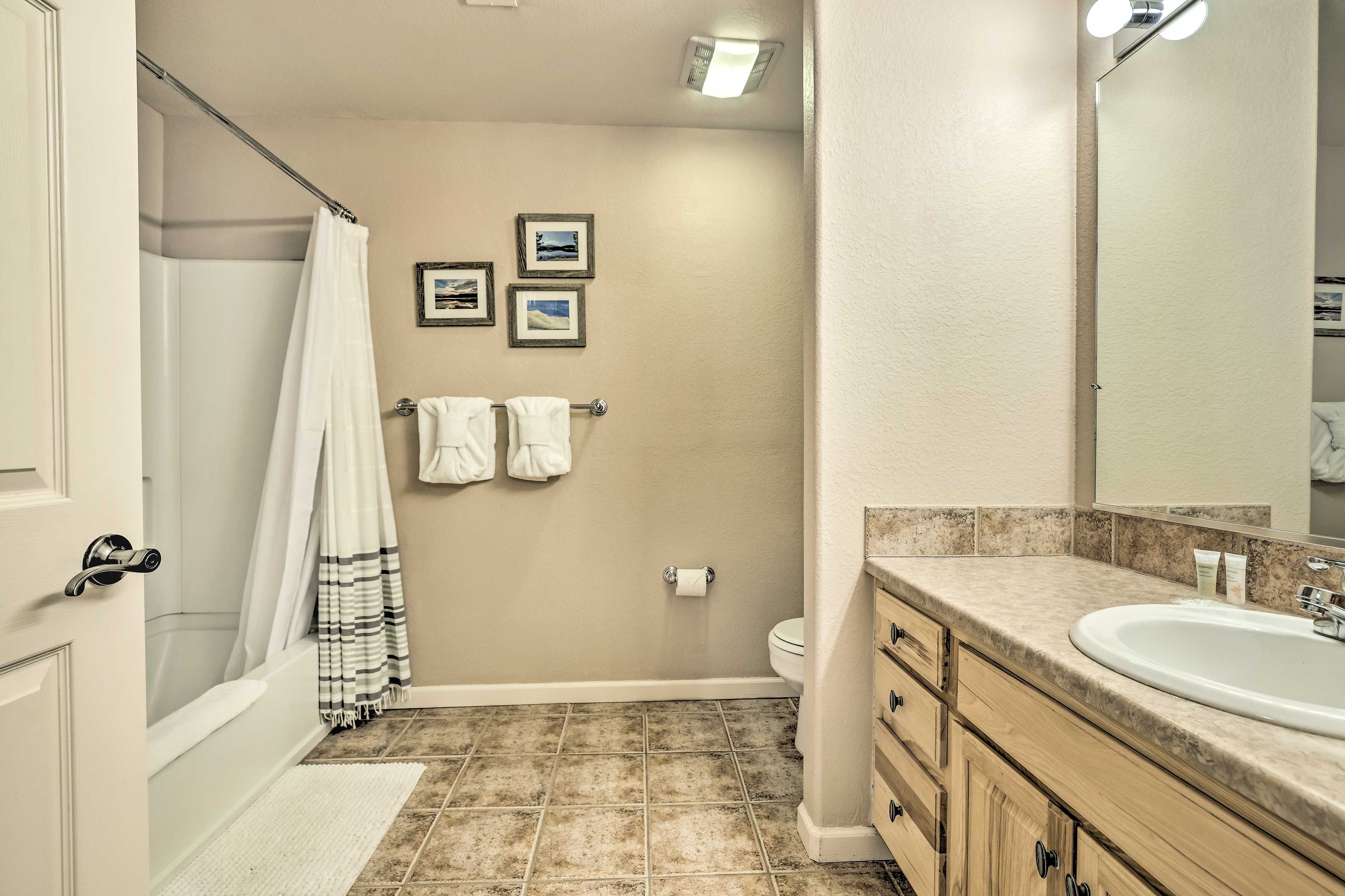 A bathroom with a bathtub, a toilet, a sink, and a mirror. There are towels hanging on a rack and pictures on the wall.
