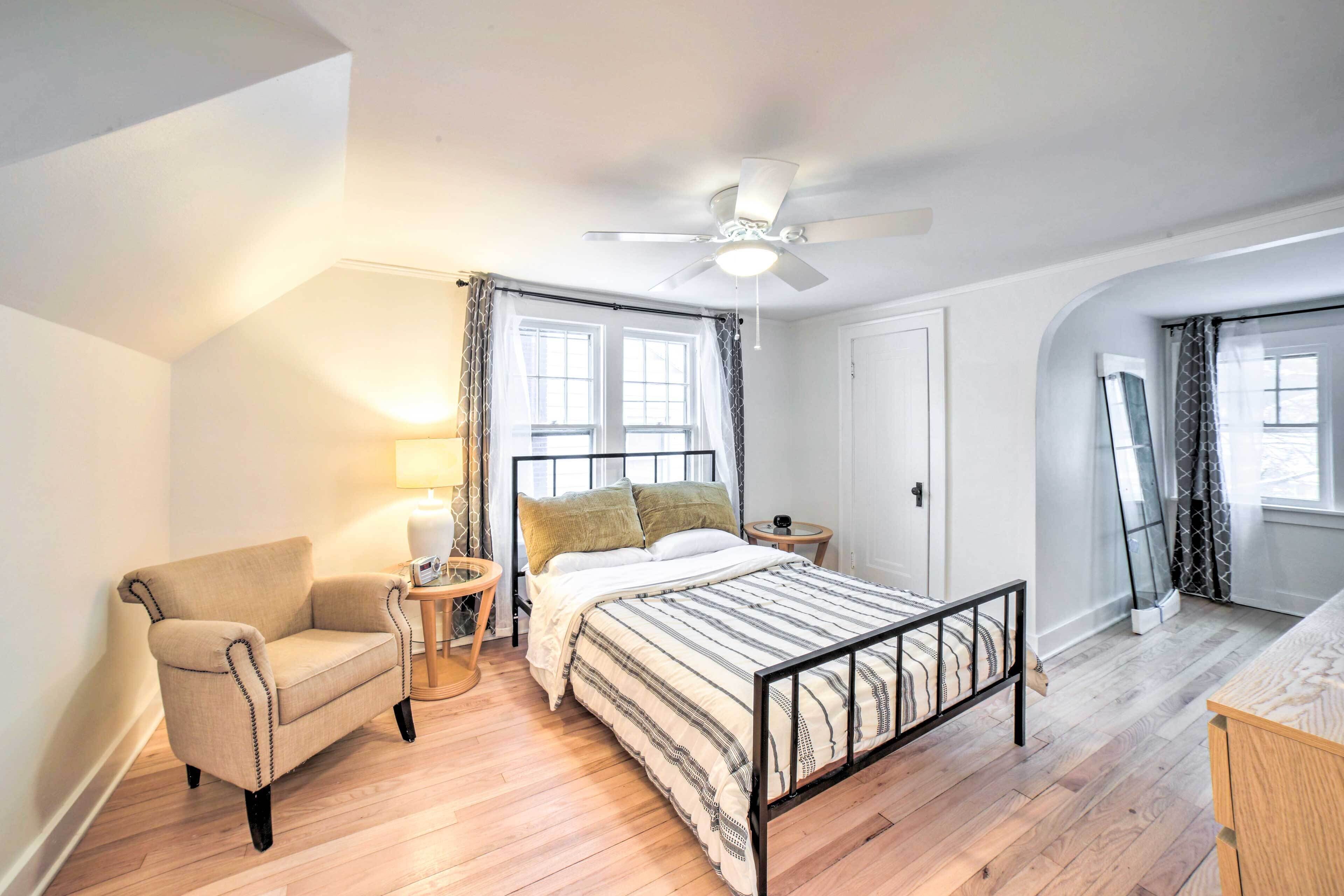 A bedroom with a bed, a chair, a ceiling fan, and a window with curtains.
