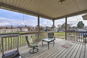 En overdækket terrasse med to stole og et bord, der vender ud mod en baghave med en trampolin og et legesæt.