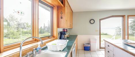 A kitchen with a large window, a sink, cabinets, and a view of the outdoors.