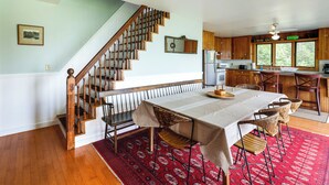 Uma área de refeições com escada de madeira, mesa de jantar posta com cadeiras e cozinha ao fundo.