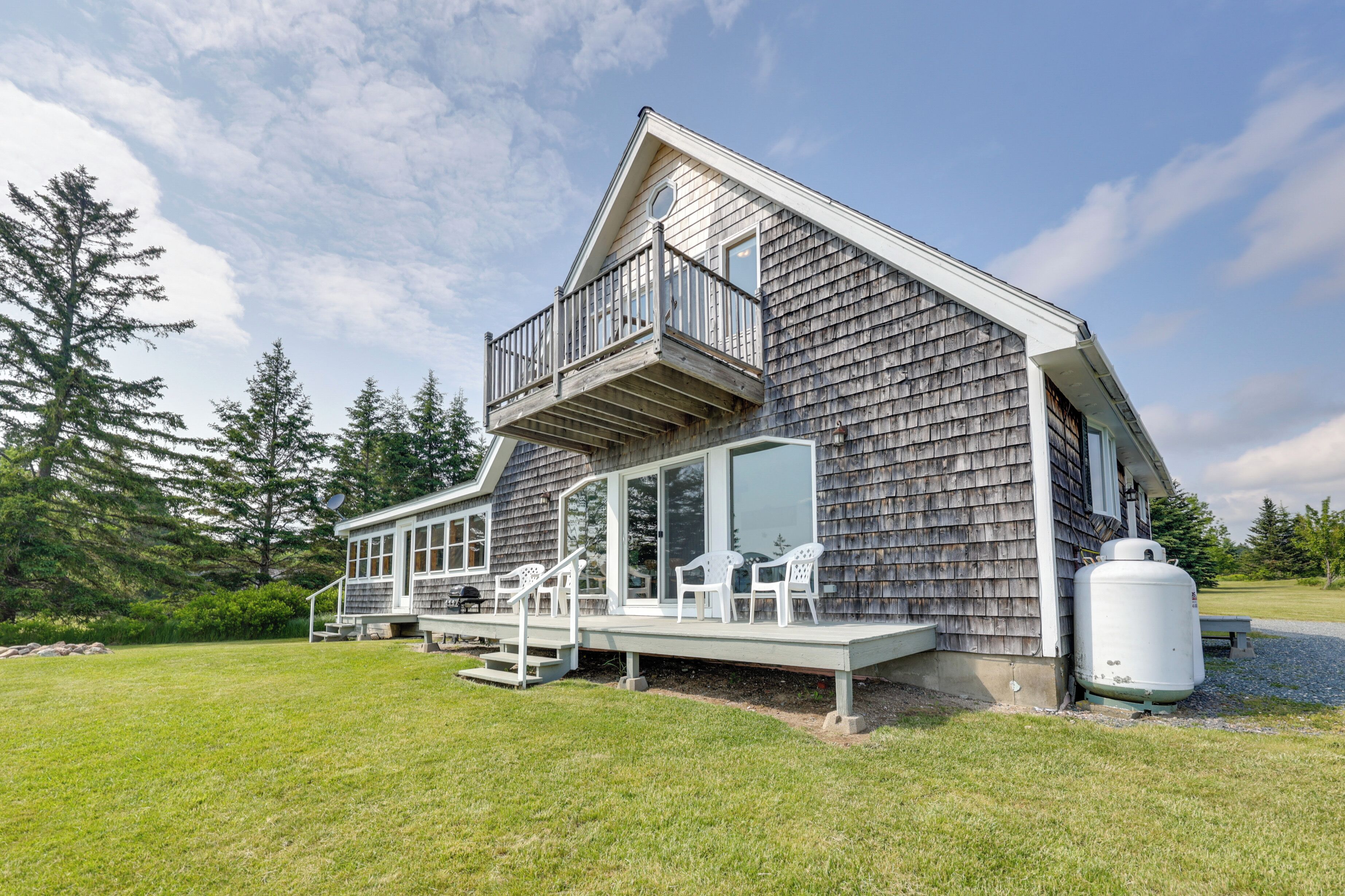 A two-story house with a balcony, a deck with chairs, and a large water tank.