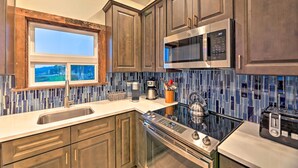 A modern kitchen with dark wooden cabinets, a stainless steel microwave, a built-in oven, and a large window overlooking a scenic view. - Sanderling Sea Cottages, Unit 5 w/ Ocean Views! (Waldport)