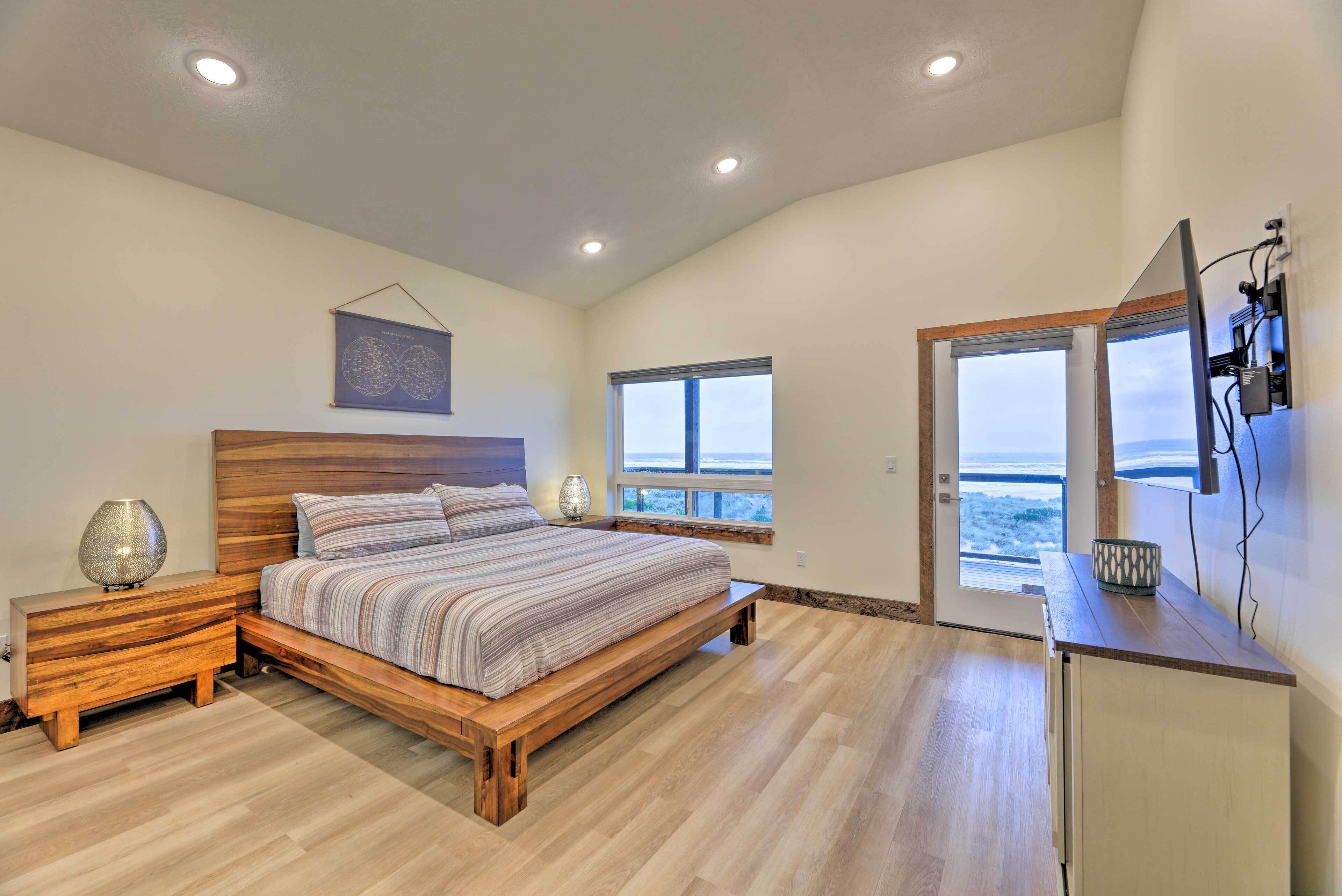 Quarto com cama de madeira, mesa de cabeceira, abajur e vista para o mar através de uma janela.