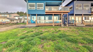 A modern two-story house with a balcony, large windows, and a grassy yard. - Sanderling Sea Cottages, Unit 5 w/ Ocean Views! (Waldport)