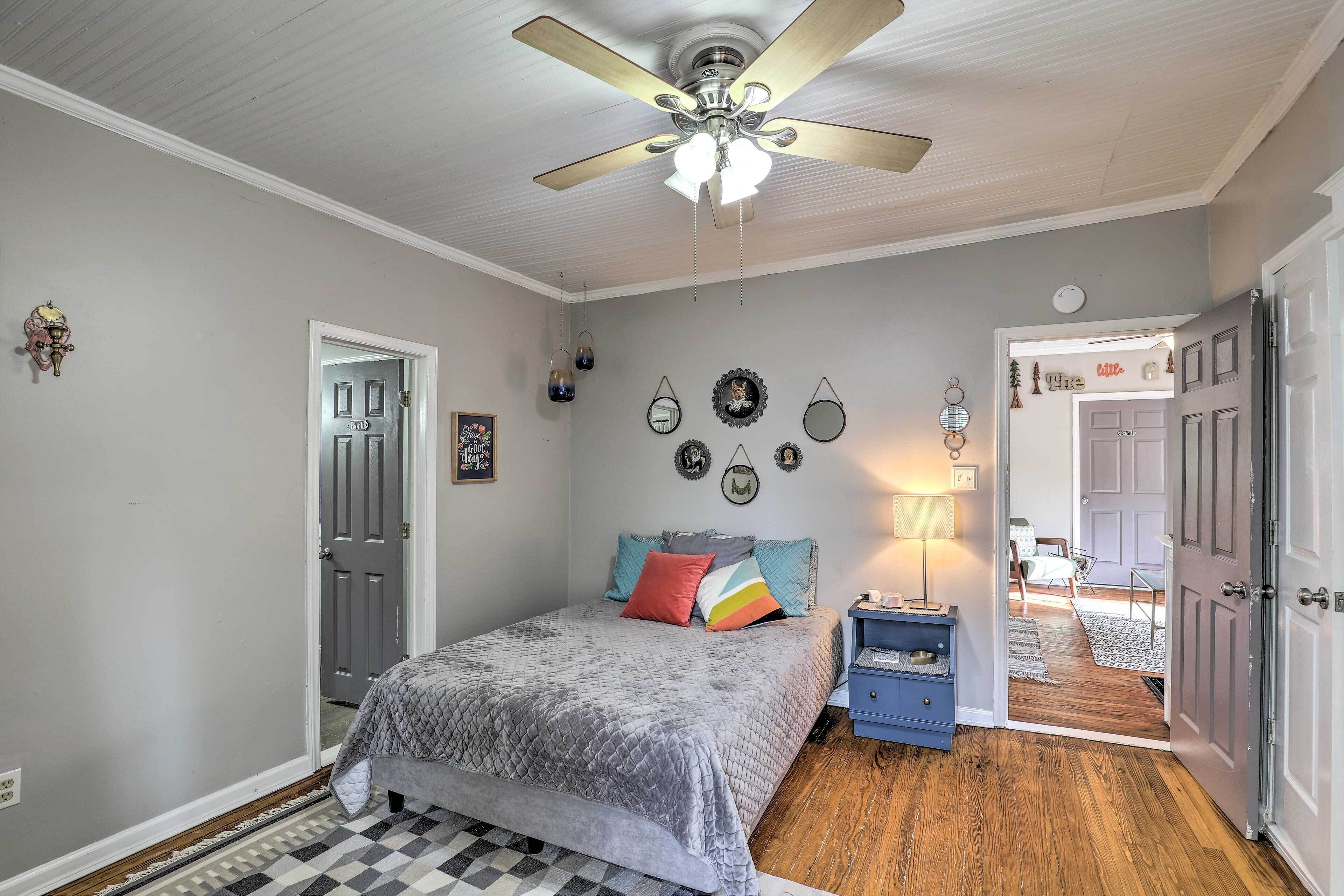 A bedroom with a bed, a ceiling fan, a nightstand, and a door leading to another room.