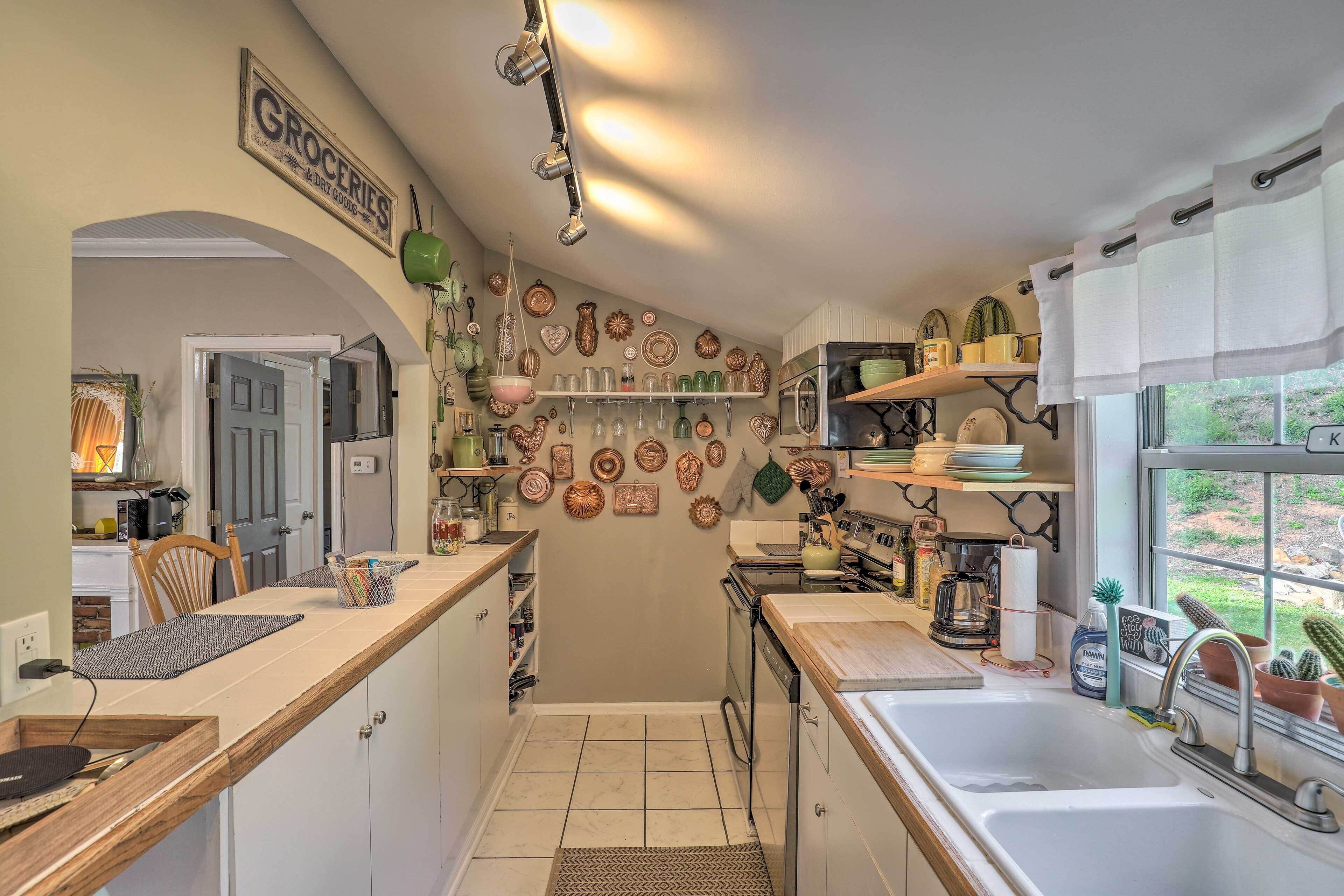 Een compacte keuken met een houten aanrecht, een spoelbak en een fornuis. Er hangen decoratieve borden aan de muur en een bordje met de tekst 'Groceries'.