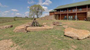Una cabaña con fachada de piedra, revestimiento de madera y un balcón con vistas a un área verde con rocas grandes y un árbol.