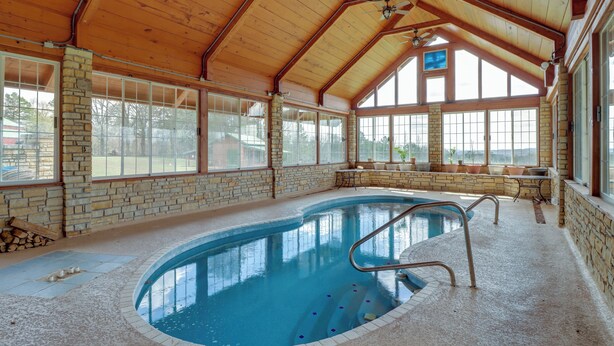 Una piscina interior con techo de madera, paredes de piedra y grandes ventanales.