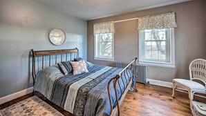 A bedroom with a wooden bed, a clock on the wall, two windows with curtains, and a chair. - Stevens Vacation Rental ~ 14 Mi to Lancaster (Stevens)