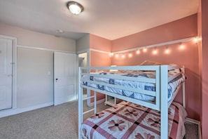 A bunk bed with a quilt, a door, and string lights on the wall.