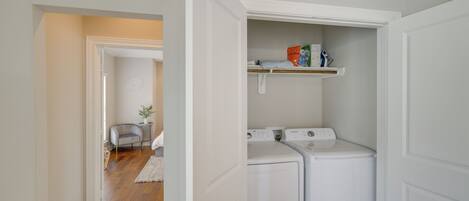 A laundry room with two white washing machines and a shelf above them.