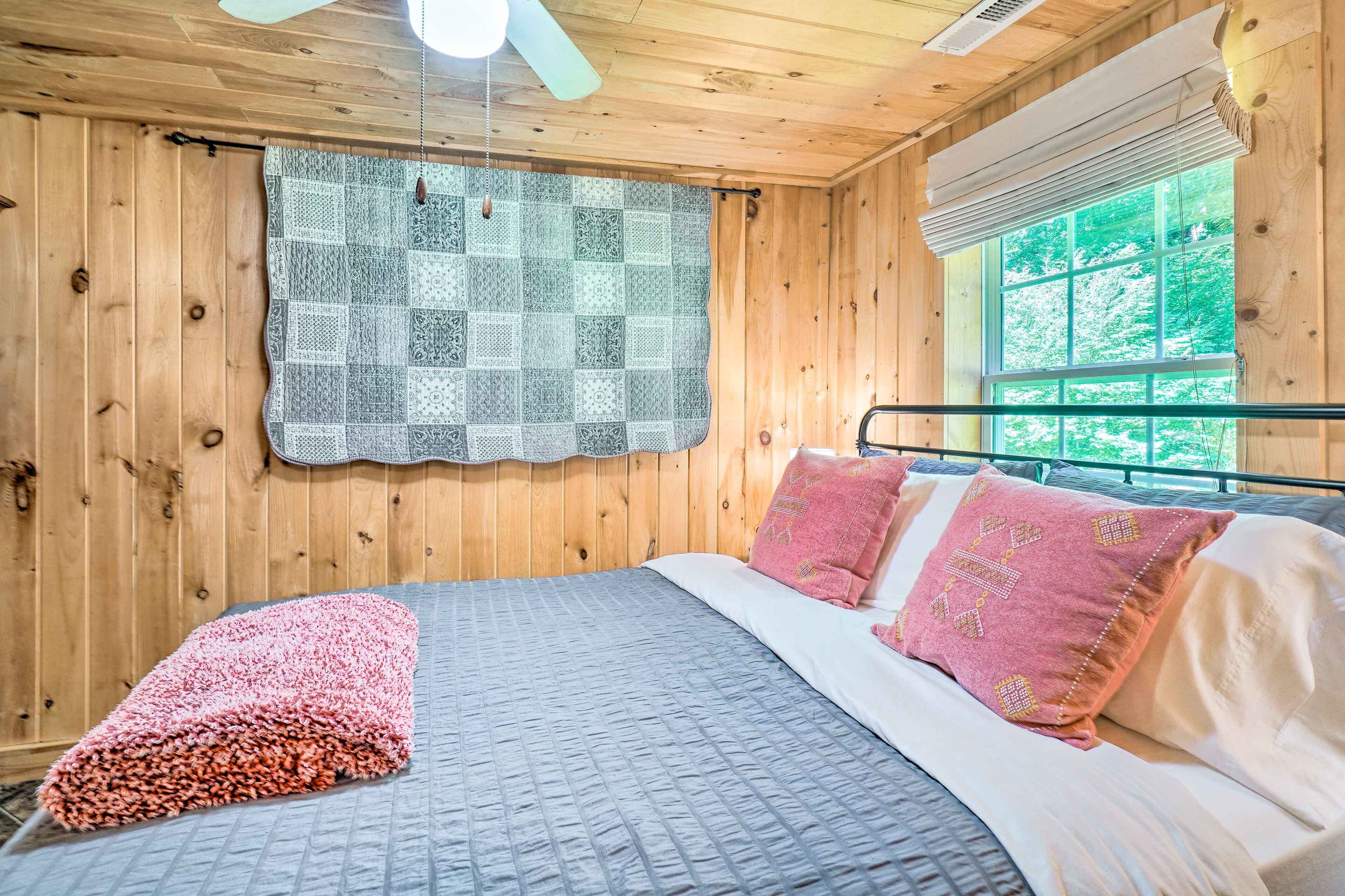 A wooden cabin bedroom with a bed, a quilt, and a window with a view of trees.