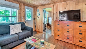 A cozy cabin interior with a wooden ceiling, a gray sofa with a decorative pillow, a wooden dresser with drawers, and a television on top. - 'the Creek' Winfield Gem: 73 Acres of Privacy (Winfield)