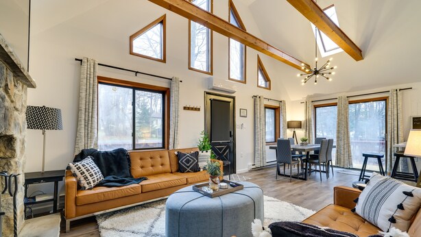 A spacious living room with a high ceiling, large windows, and a fireplace. - Poconos Chalet With Lake & Pool Access! (Tobyhanna)