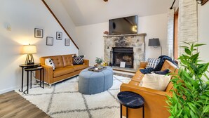 A cozy living room with a stone fireplace, a sofa, ottoman, and a coffee table. - Poconos Chalet With Lake & Pool Access! (Tobyhanna)