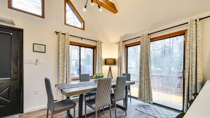 A dining area with a wooden table and chairs, large windows with curtains, and a view of the outdoors. - Poconos Chalet With Lake & Pool Access! (Tobyhanna)